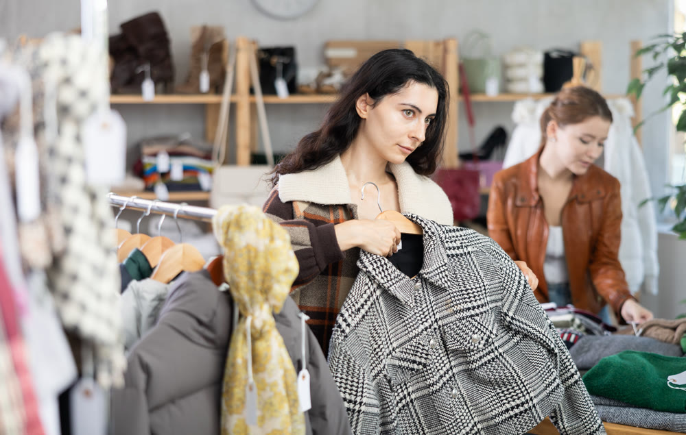 Female shopper chooses and try beautiful checkered coat-jacket in clothing store