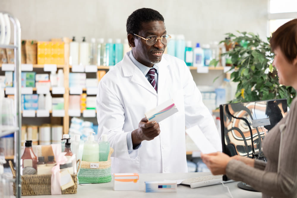 In drug store, African man at counter sells medication to customer