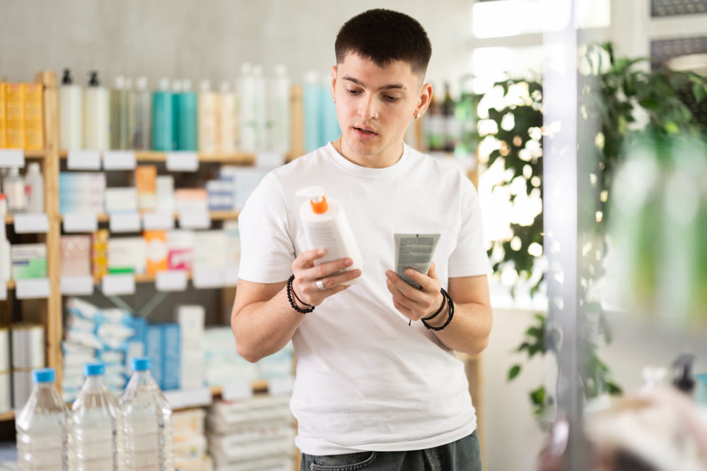 Young man choosing creams in pharmacy