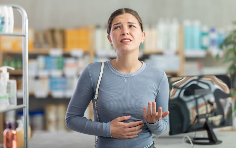 Woman with stomach pain looking for medication at drugstore