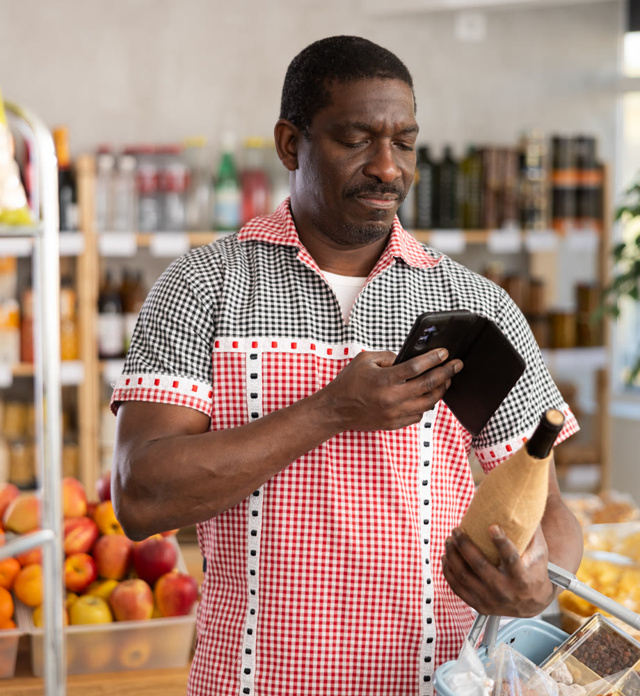 African man customer at shop scans QR code on wine bottle using phone camera
