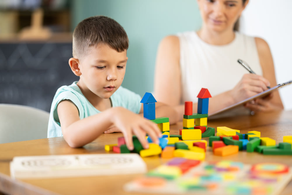 Boy at table collects figures from cubes, builds towers from wooden cubes.
