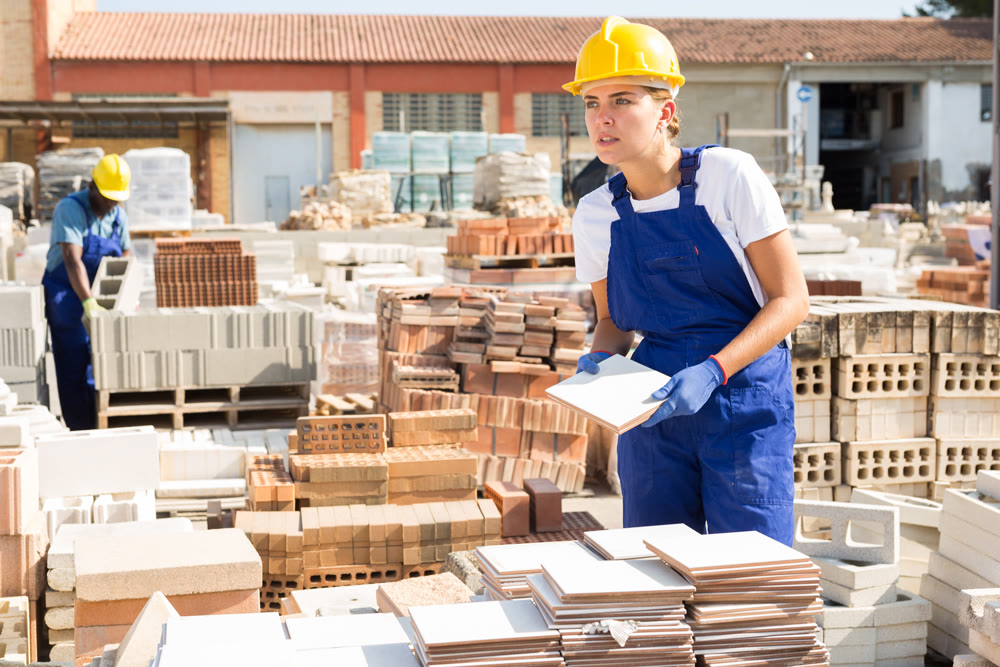 Young attentive female worker lays tiles in a warehouse