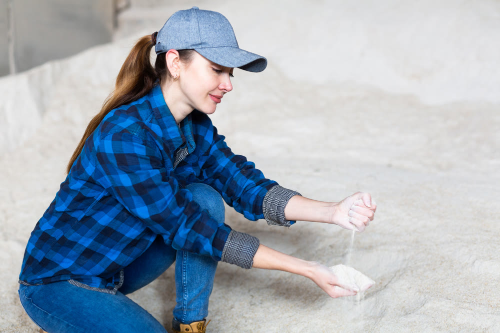 Young woman livestock breeder checking quality of soybean meal in farm storage