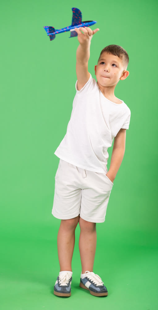 Boy in white t-shirt and shorts playing with airplane model on green background