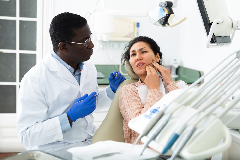 Woman patient who came to an appointment with a male dentist is sitting in a dental chair in clinic office, showing which side of her tooth aches