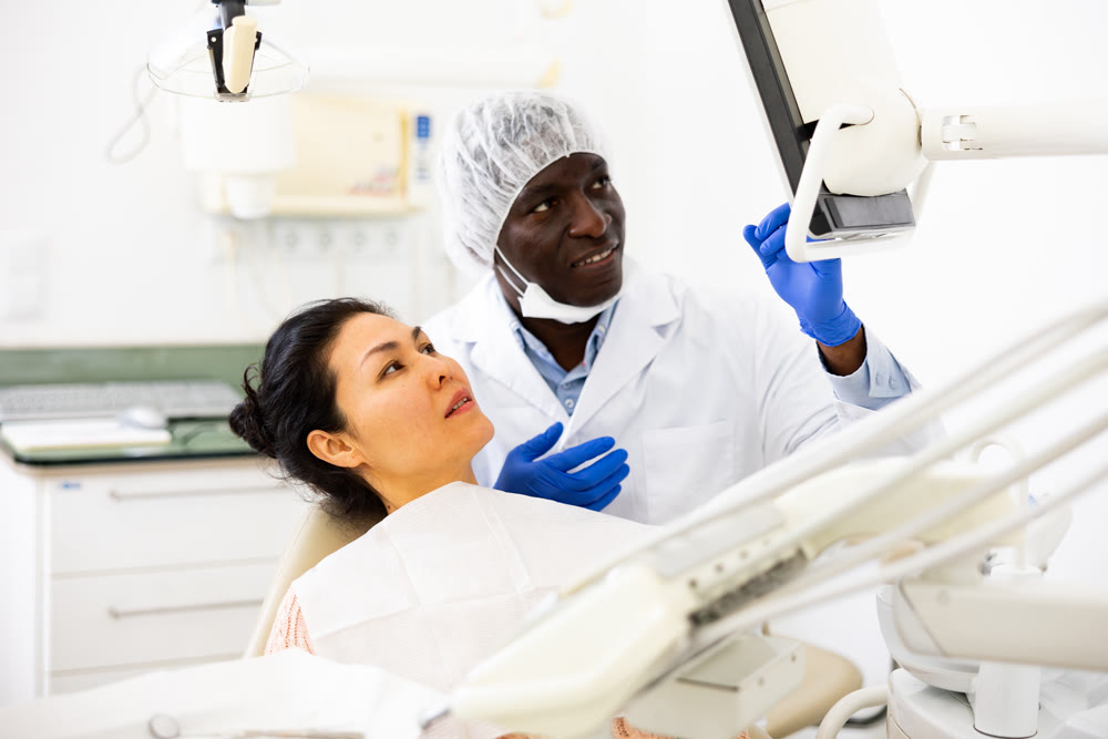 Man dentist pointing at display to show information to patient