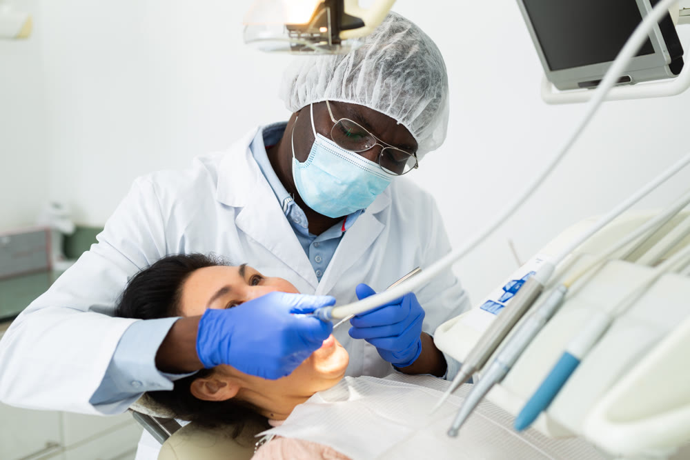 Professional dentist performing teeth treatment to woman at dental clinic