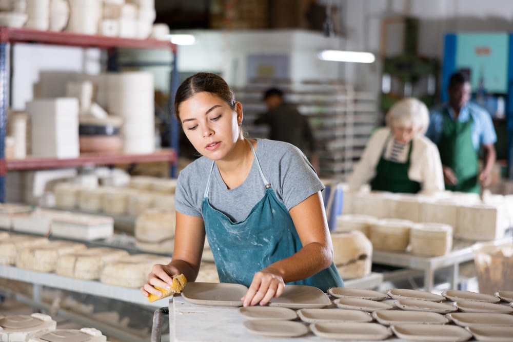 Female ceramist wiping clay bowl with sponge in ceramic factory