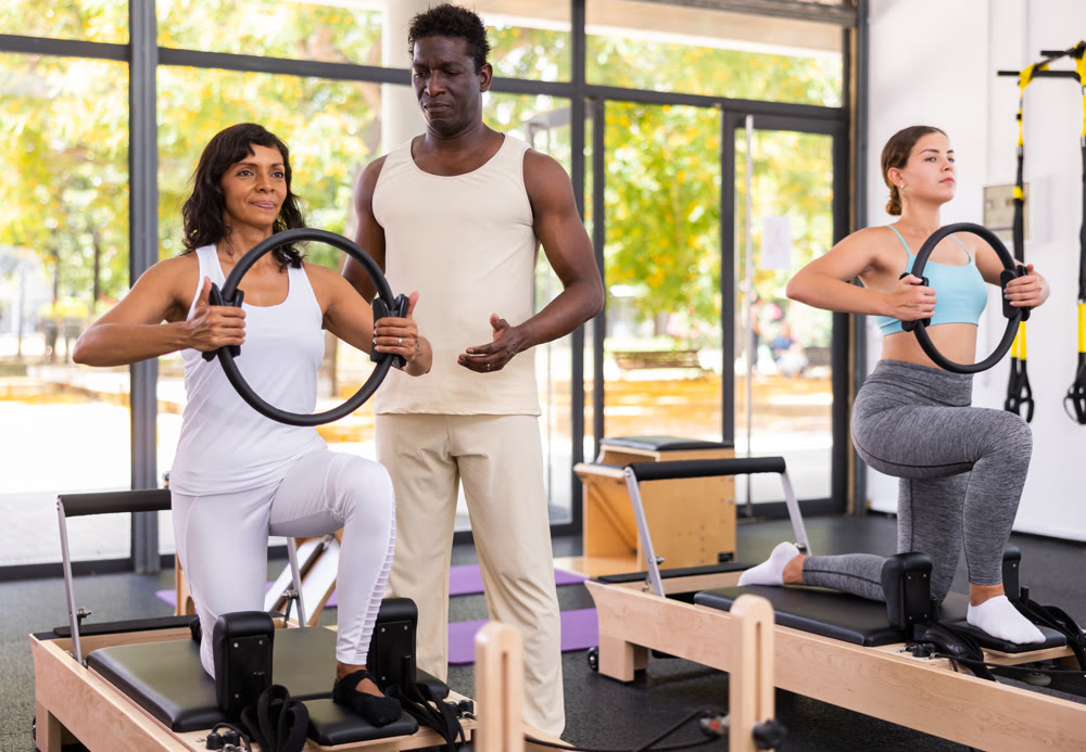 Two women having pilates workout on reformers with trainer