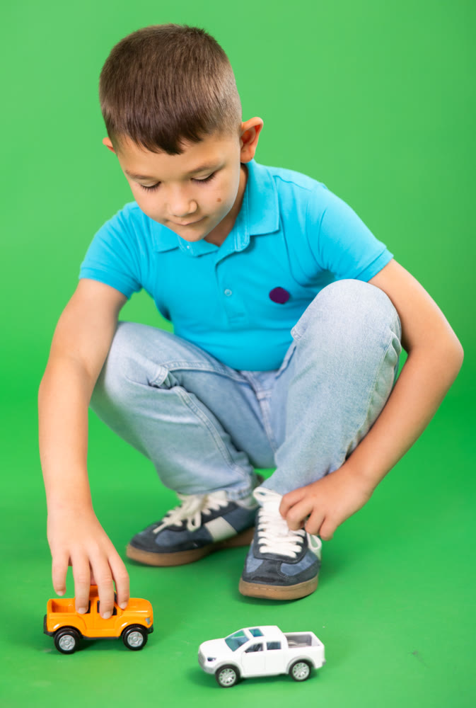 Boy playing with toy cars on green background