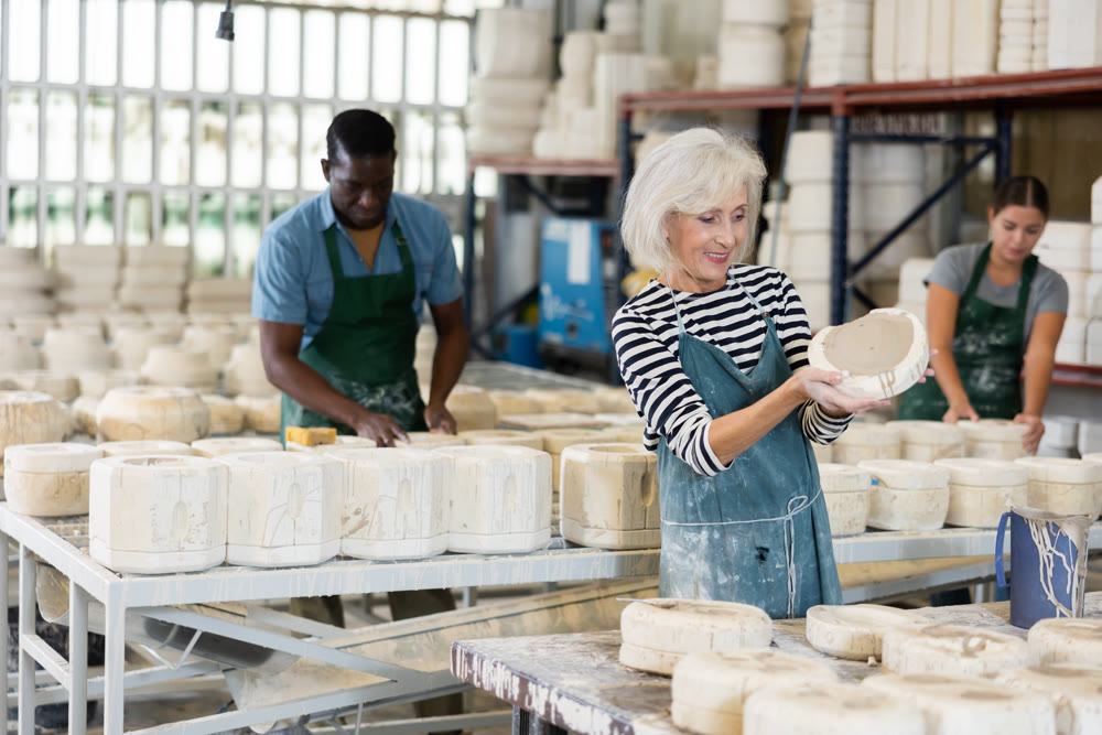 Elderly worker demonstrates half of plaster mold for pottery.
