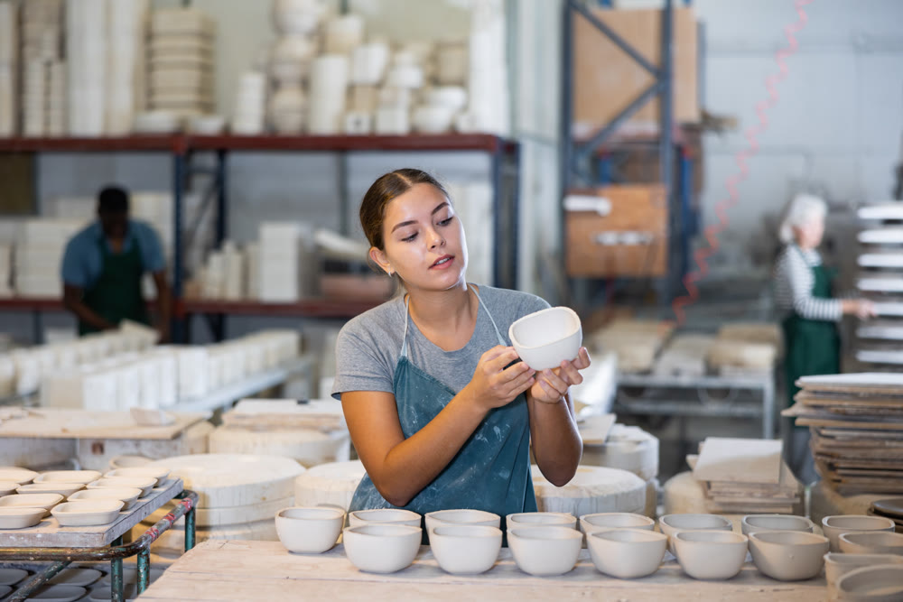 Young woman foreman checks the quality of pottery in the workshop for production of clay products