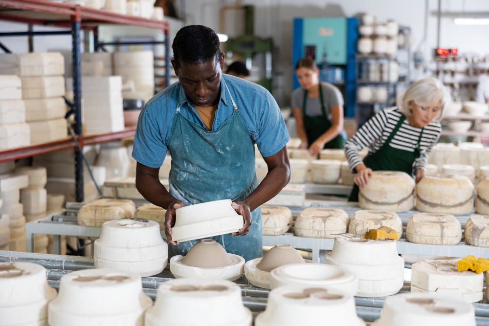 African american worker in pottery factory removes the first half of plaster mold from clay bowl