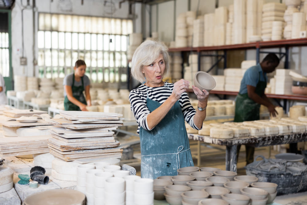 Mature craftswoman checking quality of pottery in pottery factory