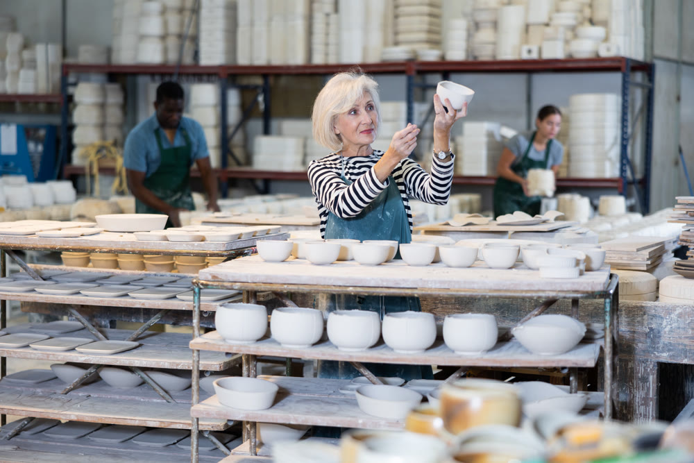 Mature craftswoman checking quality of pottery in pottery factory