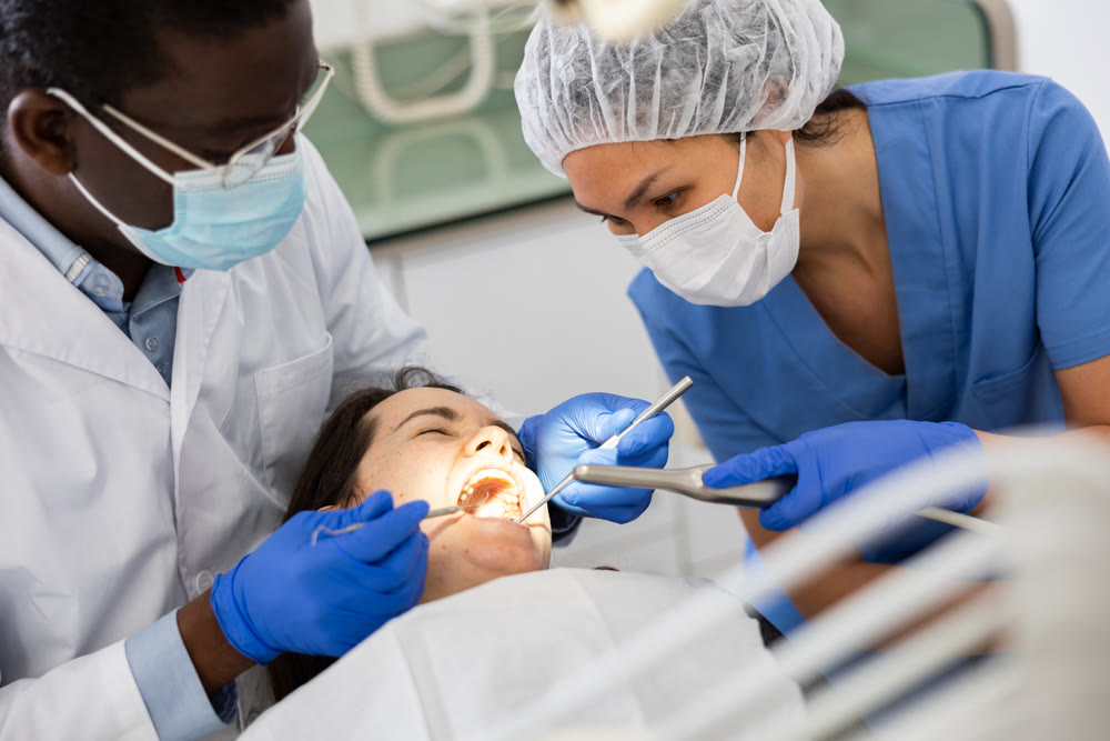 Focused stomatologist with female assistant treating teeth to woman patient