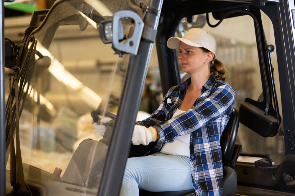 Young female worker of warehouse working on forklift truck