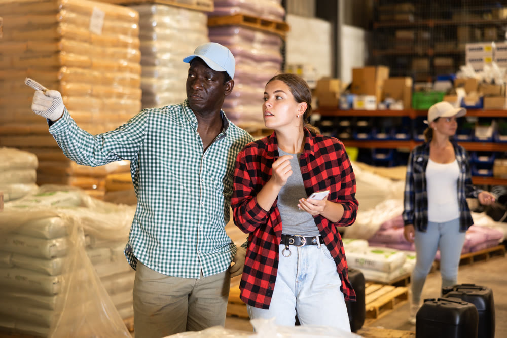 Man talking with young woman in warehouse and pointing with his hand at bags with products
