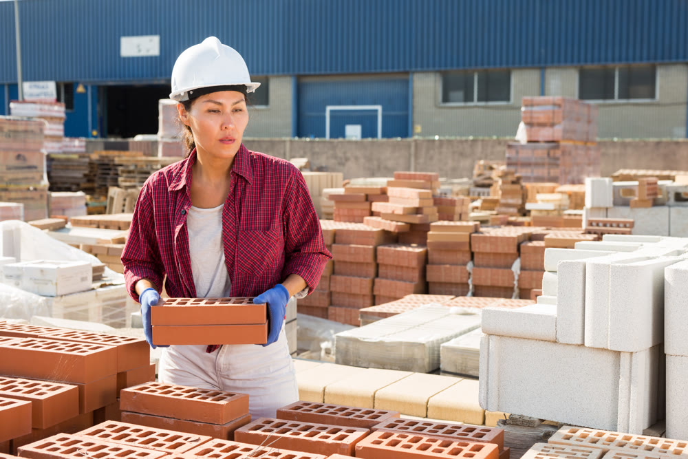 Asian worker stacking bricks in warehouse of building materials on an open-air site