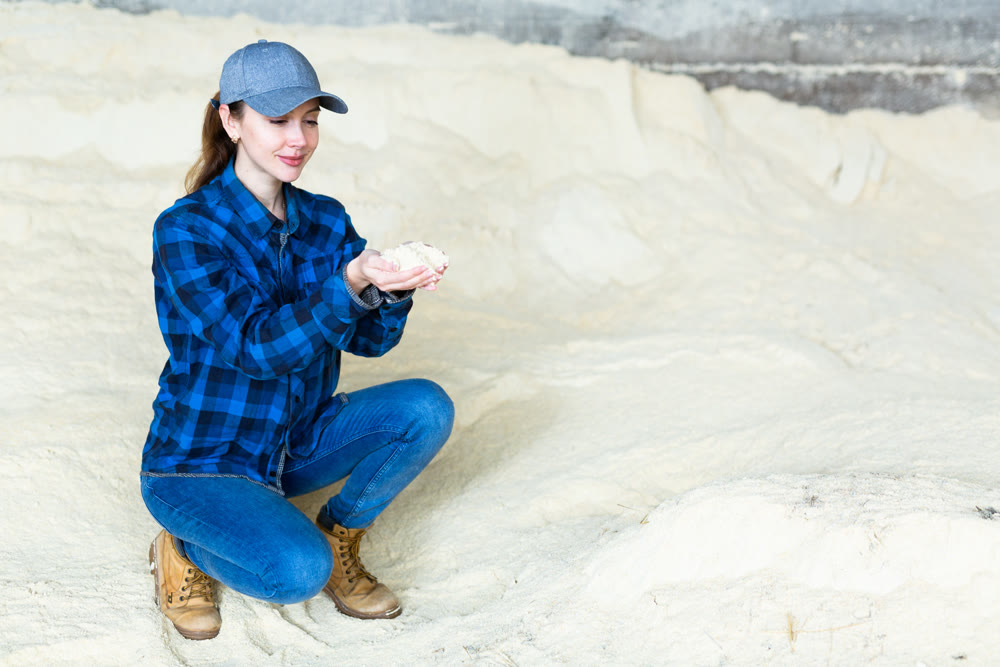 Woman farmer holding handful of corn flour, in animal food storage
