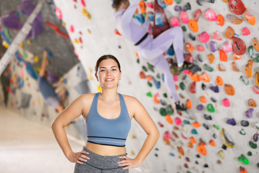 Smiling sporty girl posing near climbing wall at bouldering gym