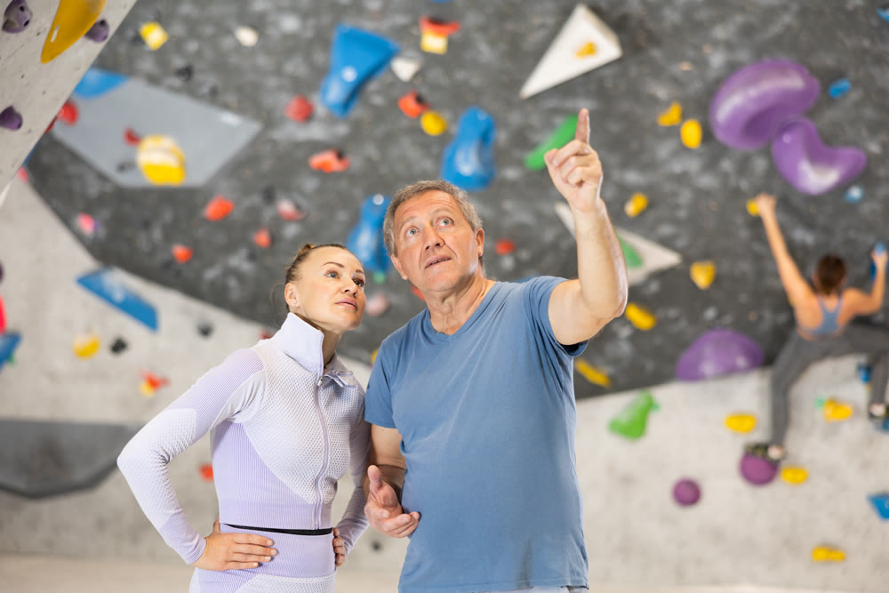 Trainer giving instructions to man on wall climbing at bouldering gym indoor