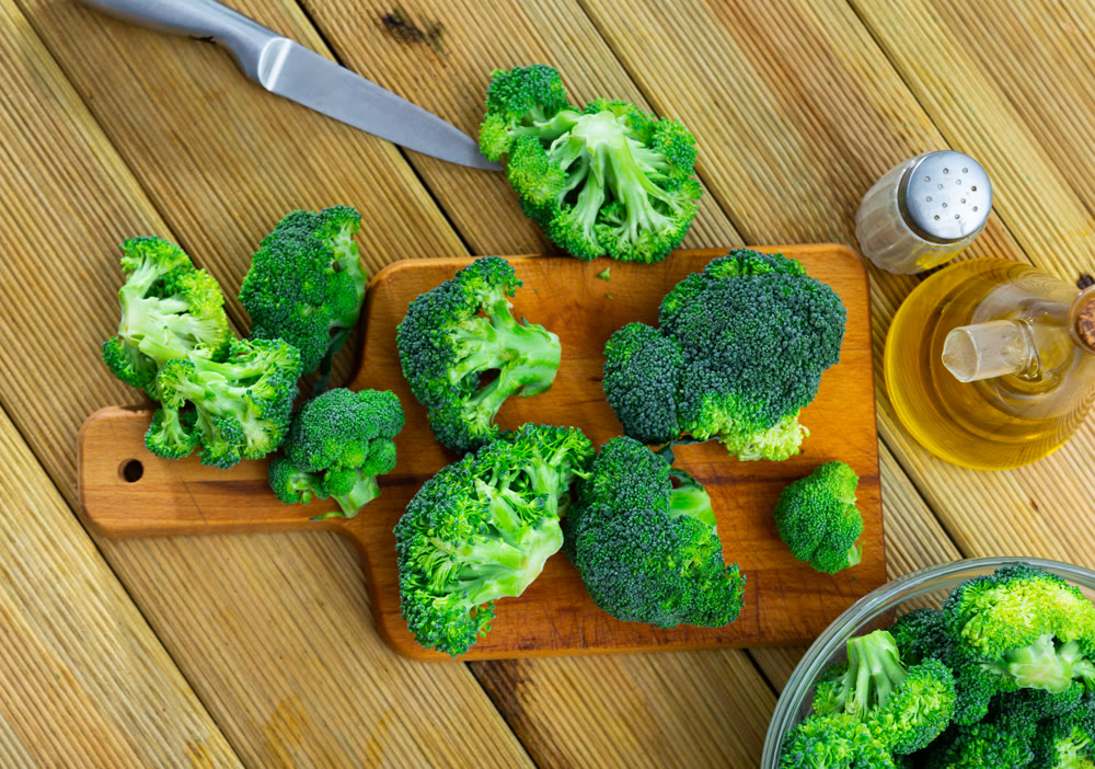 Florets of fresh raw broccoli on wooden cutting board with oil and spices