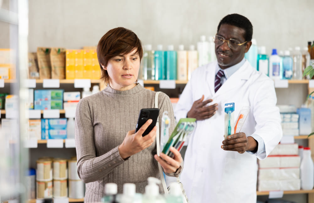 Woman in pharmacy scans QR code on toothbrush. African pharmacist in background