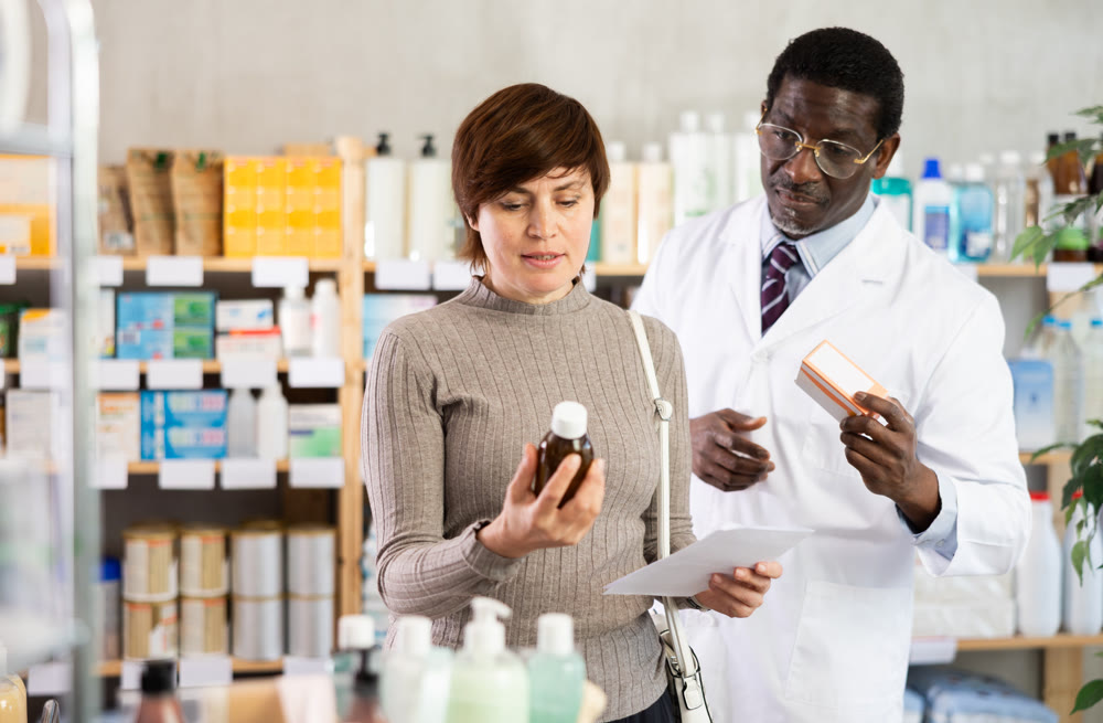 Woman choose buy antitussive syrup at pharmacy. African man in background