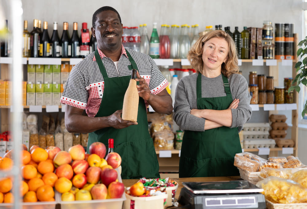 African man and European woman sellers stands and work in trading hall of store
