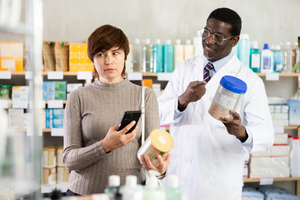 Woman in pharmacy scans QR code on infant formula. African man pharmacist in background