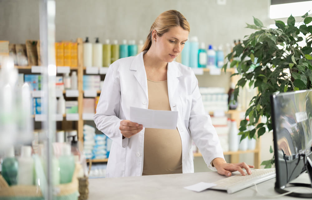 Pregnant woman pharmacist checking prescription on computer