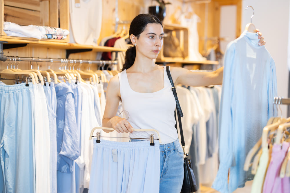 Girl in clothing store chooses several items of clothing, makes up summer look.