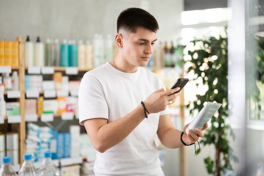 Young man choosing skin care lotion, gel or medical ointment, scanning qr code in drugstore