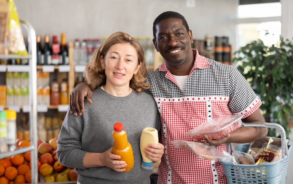 Portrait of couple with various products in hands continuing shopping in grocery department of supermarket