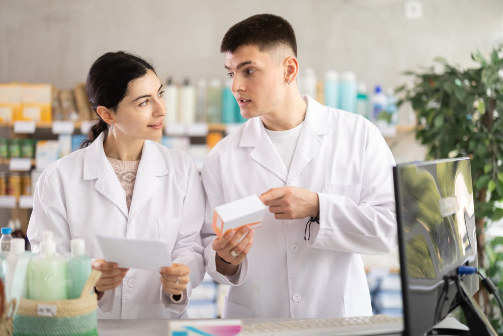 Two male and female pharmacists attentively stocktaking medicines with computer at pharmacy shop
