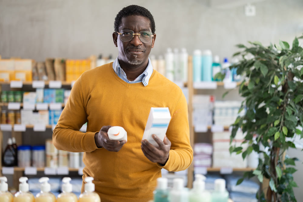 Male buyer in glasses attentively chooses skin cream at drugstore