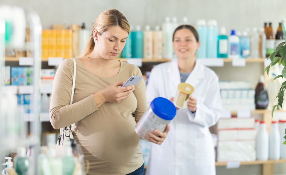 Expecting mother checking baby formula ingredients with phone at drugstore