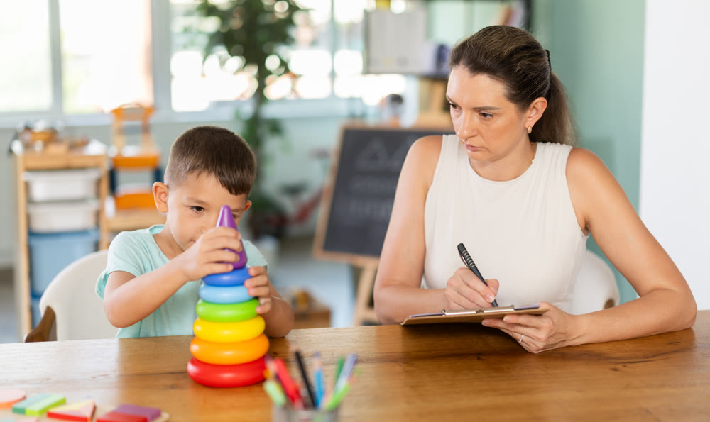 Child psychologist observing boy assembling toy pyramid