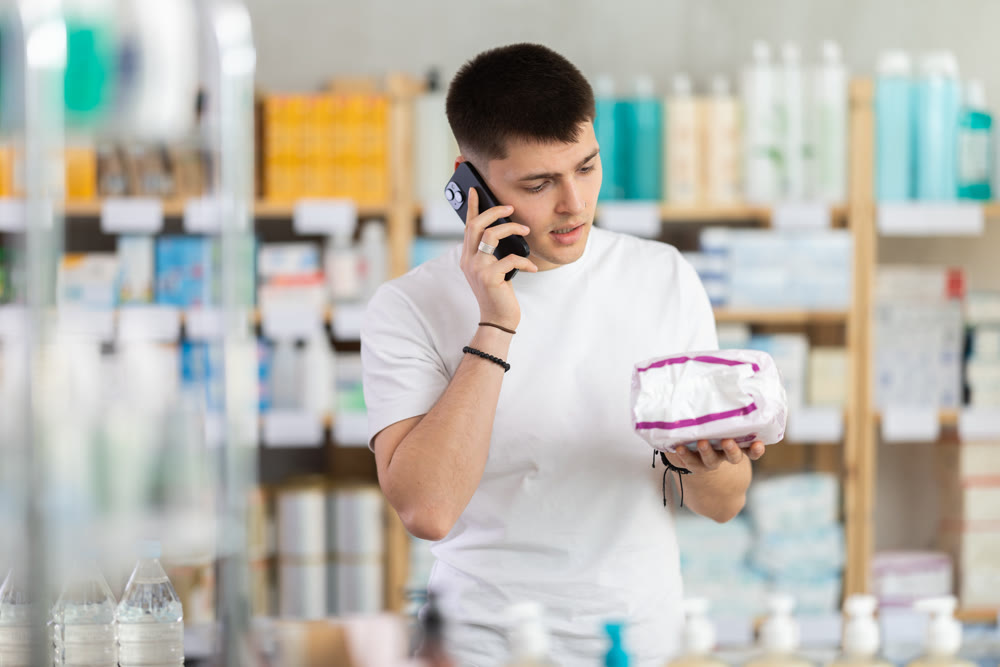 guy is holding a package of pads in his hands and making a phone call