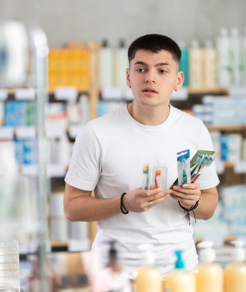 Portrait young man choosing best toothbrush at pharmacy