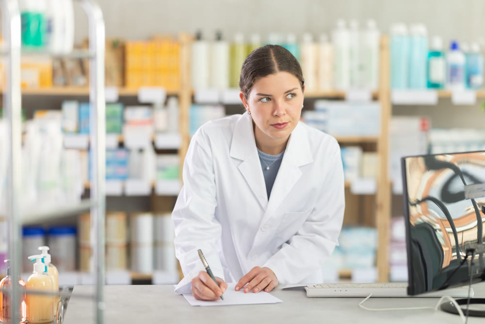 Young female pharmacist restocking using paper in drugstore