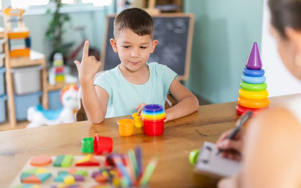 Boy collects multi colored plastic cups by placing them inside each other. Psychologist helps and observes.