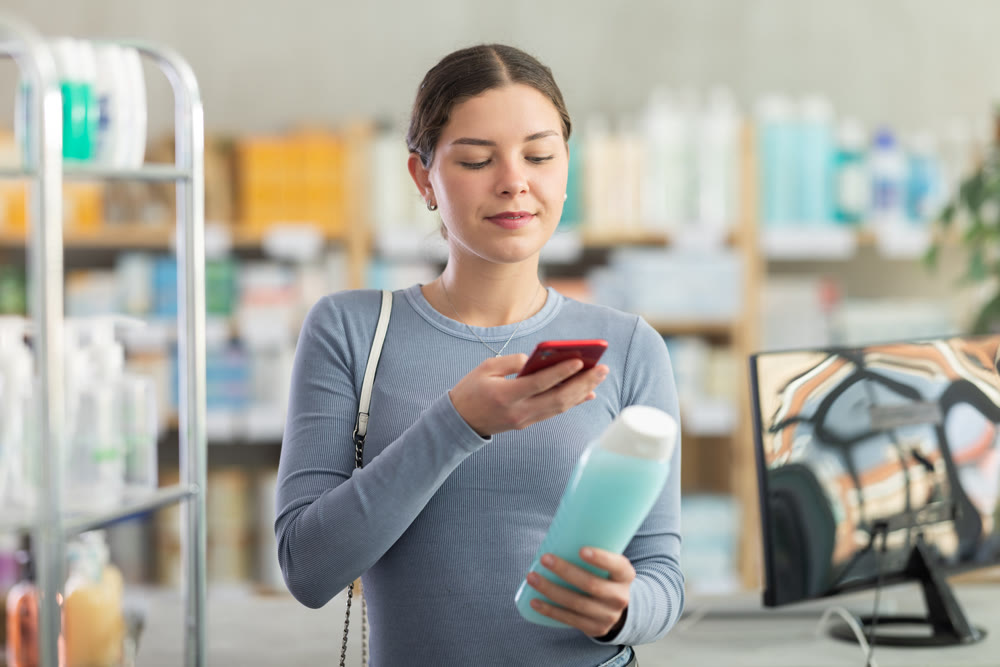 Young woman scanning QR-code on shampoo in drugstore
