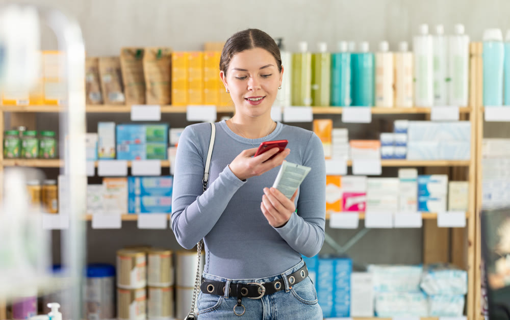 Woman researching body cream using phone at pharmacy