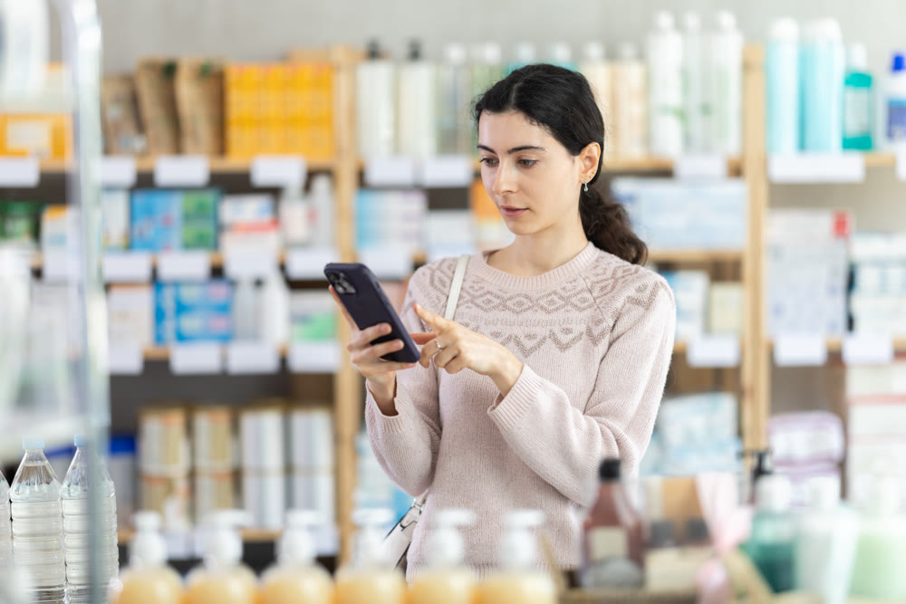 Woman choosing goods in pharmacy with phone