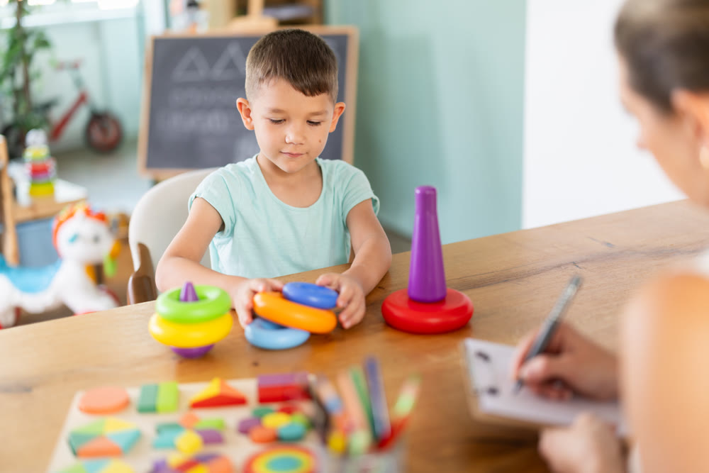Boy builds a pyramid from children circles in kindergarten under supervision of child psychologist