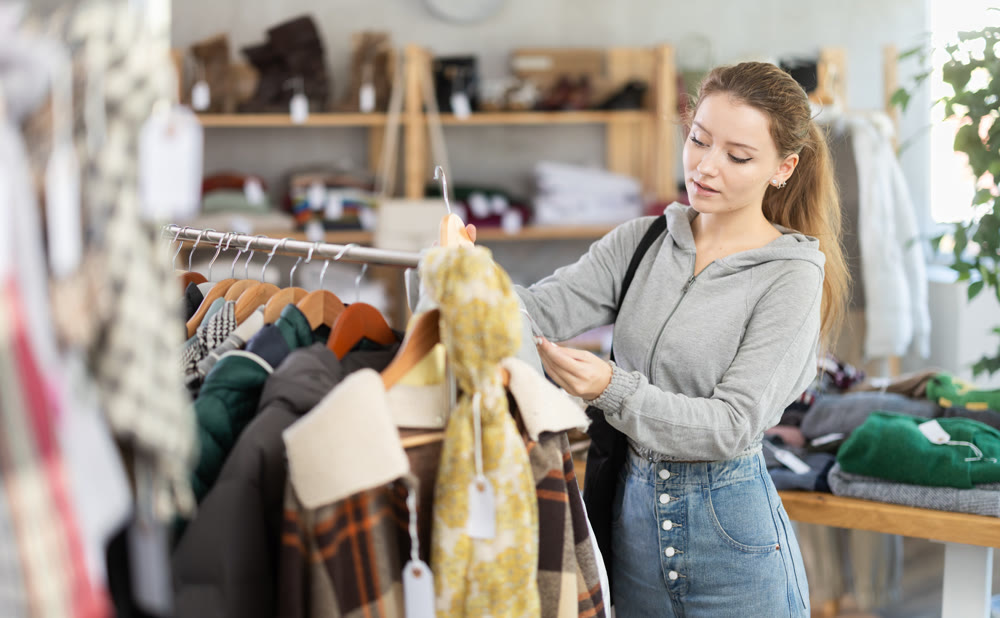 Female shopper carefully selects a fashionable jacket in clothing boutique.