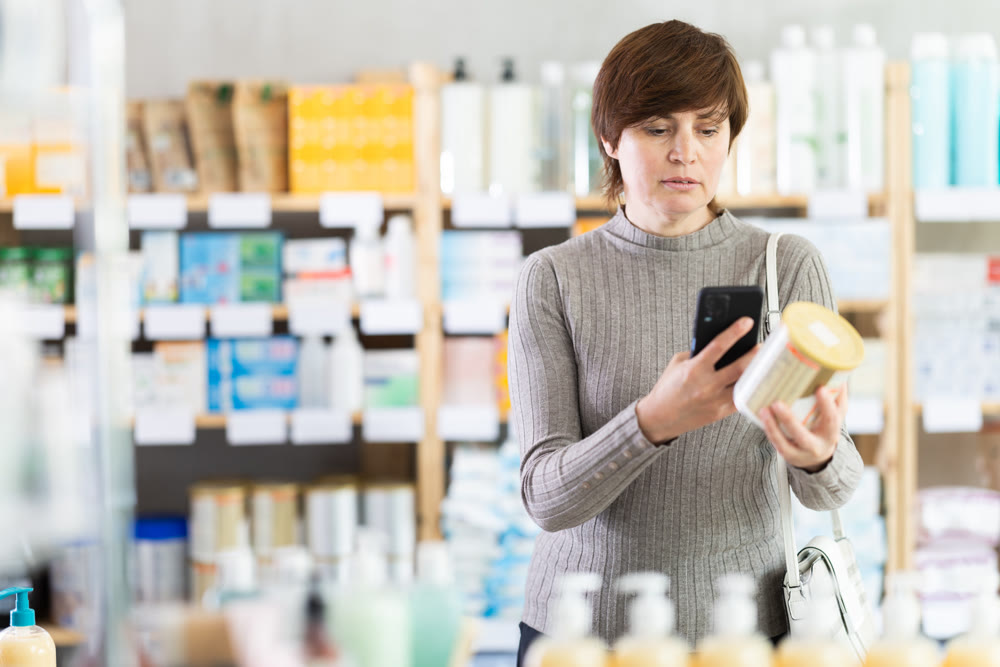 Female shopper in winter clothes scans QR code on label of food for small children using smartphone